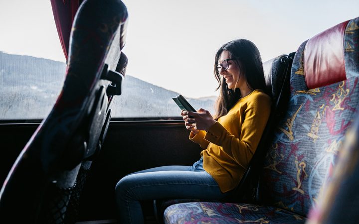 年轻美丽的白人女子在乘公共汽车旅行时阅读新闻或使用智能手机查看社交媒体。