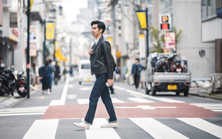 在东京市区，一名年轻的日本男子在放松的城市休息时间穿过人行斑马线。