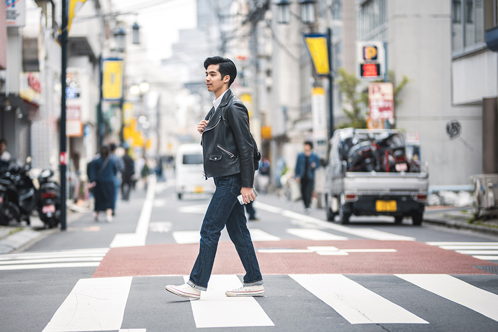 在东京市区，一名年轻的日本男子在放松的城市休息时间穿过人行斑马线。